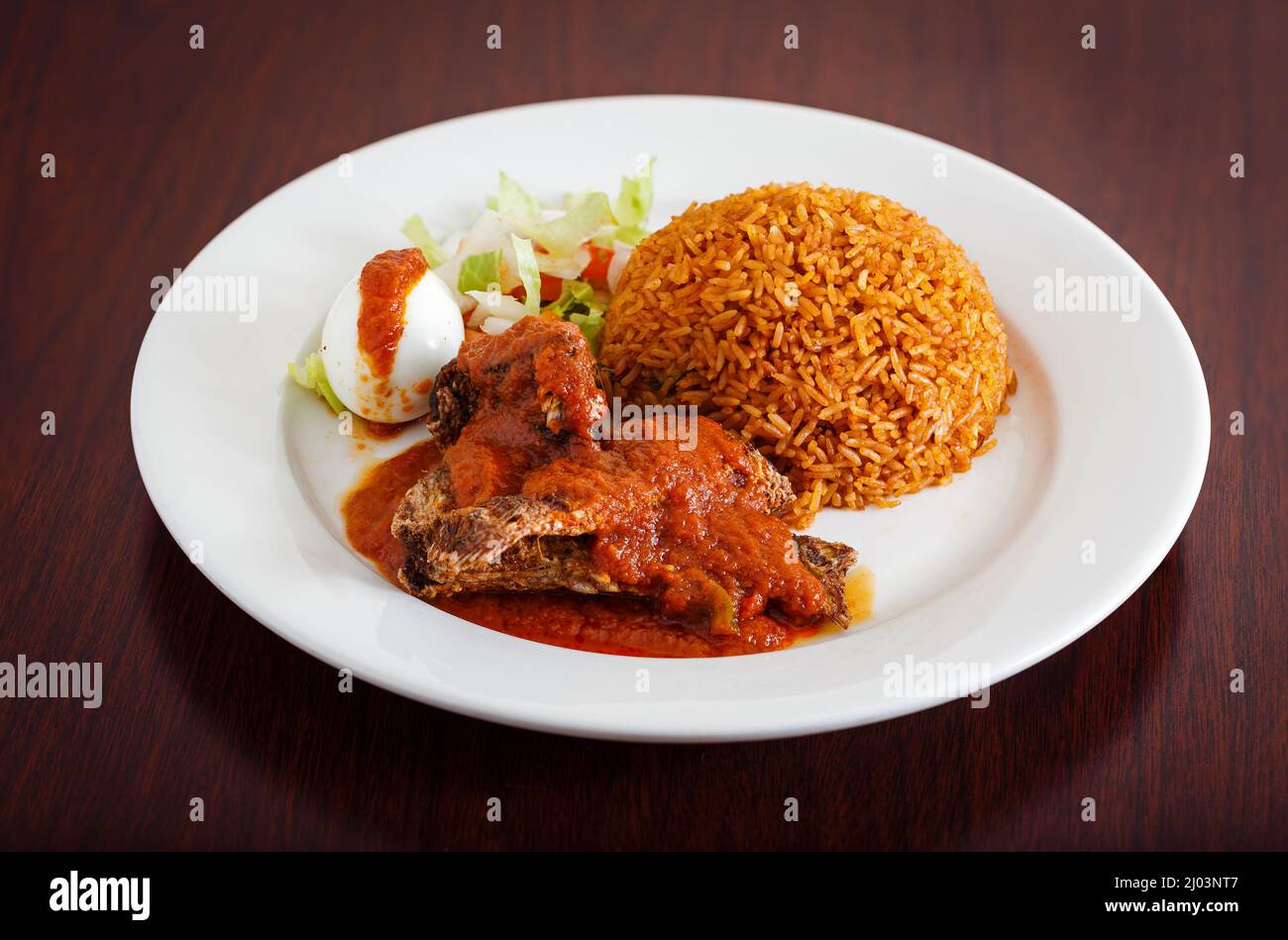 Classic Ghanaian meal of jollof rice, fish covered in red sauce, and boiled egg Stock Photo