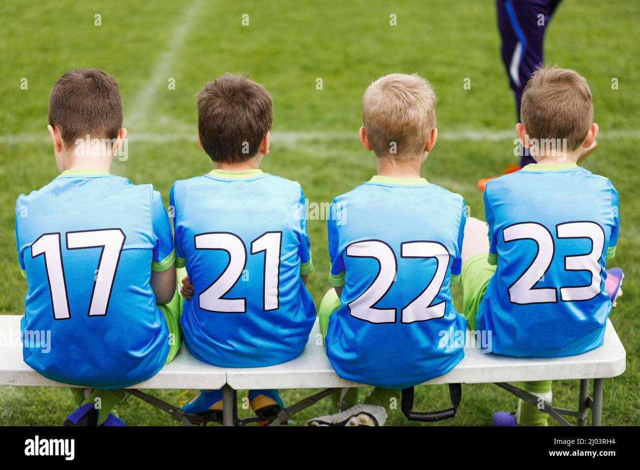 School football team. Soccer players sitting on sideline bench. Youth soccer players sitting together on substitute bench and watching match Stock Photo