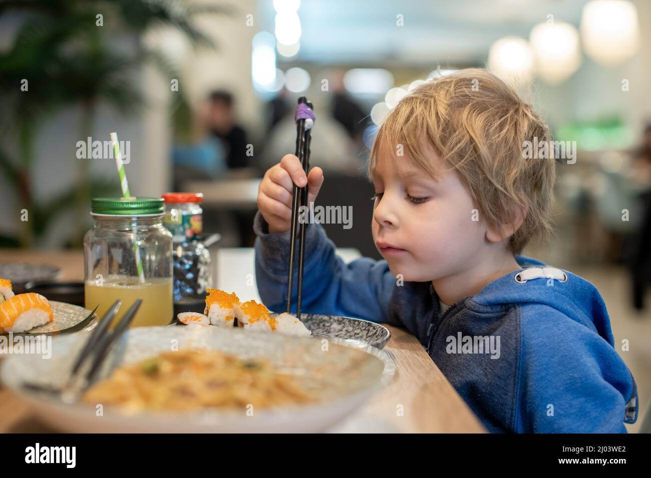 Child, eating japanese sushi and noodles with chopsticks in a restaurant, dinnertime Stock Photo