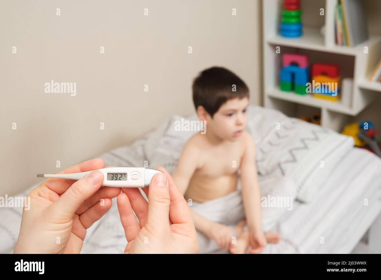 A thermometer in the hands of a pediatrician or parent with numbers of more than 39 degrees Celsius against the background of a child of 4 years Stock Photo