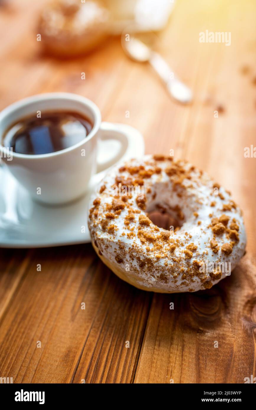 White donut with chocolate sprinkle and cup of coffee on wood table Stock Photo