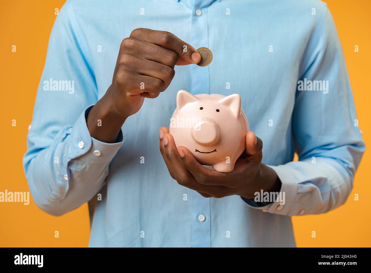 Close up of black man hand putting coin into piggy bank Stock Photo - Alamy