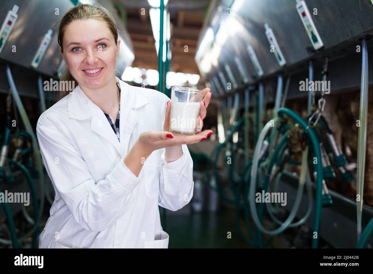 Female dairy engineer in white robe standing with glass of milk near