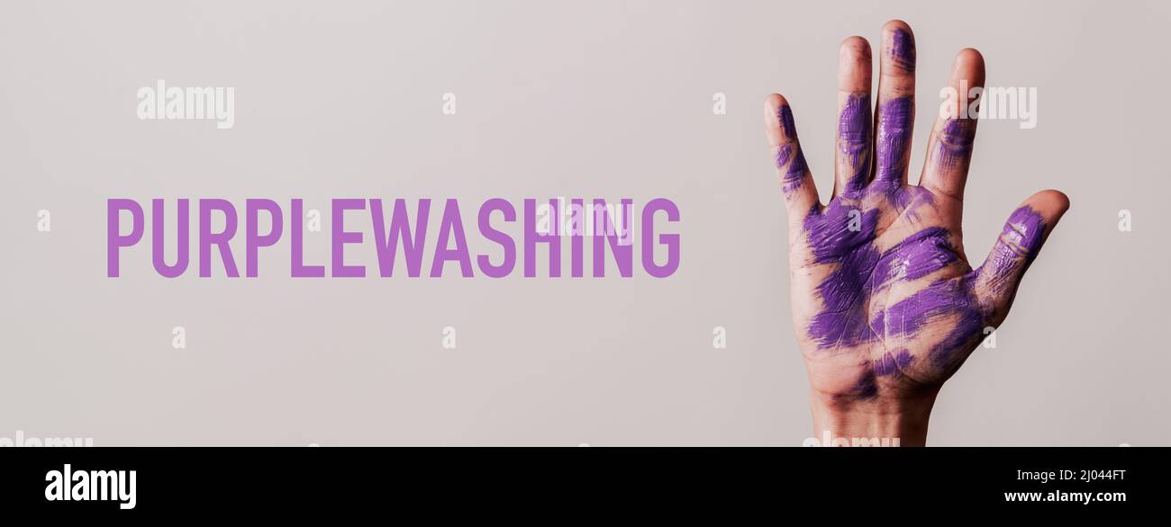 the text purplewashing and the raised hand of a man with stains of purple paint, on a gray background, in a panoramic format to use as web banner or h Stock Photo