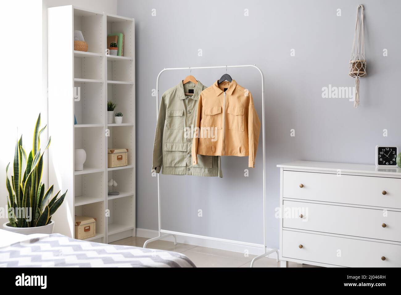 Rack with stylish jackets near light wall in bedroom Stock Photo