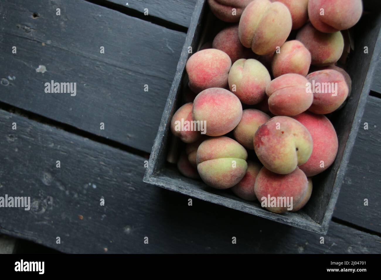 Red juicy peaches lie in a box on a vintage table. Stock Photo