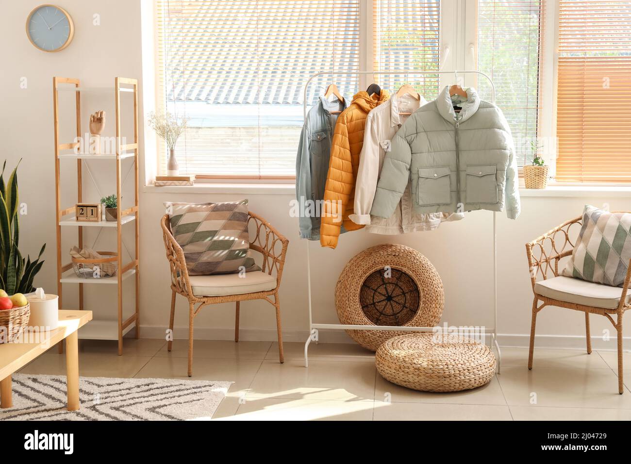 Interior of light room with armchair, shelving unit and warm jackets Stock Photo