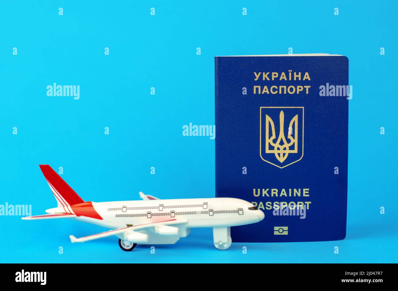 Departure of Ukrainians abroad. Ukrainian passport and toy plastic plane on a blue background, selective focus Stock Photo