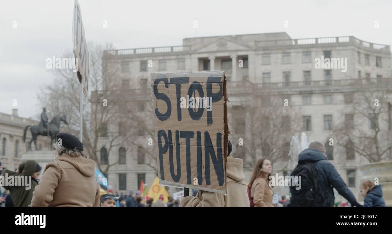 London, UK - 03 06 2022:  A woman protester walking through a crowd of people at Trafalgar Square, holding a sign, ‘Stop Putin’, in support of Ukraine. Stock Photo