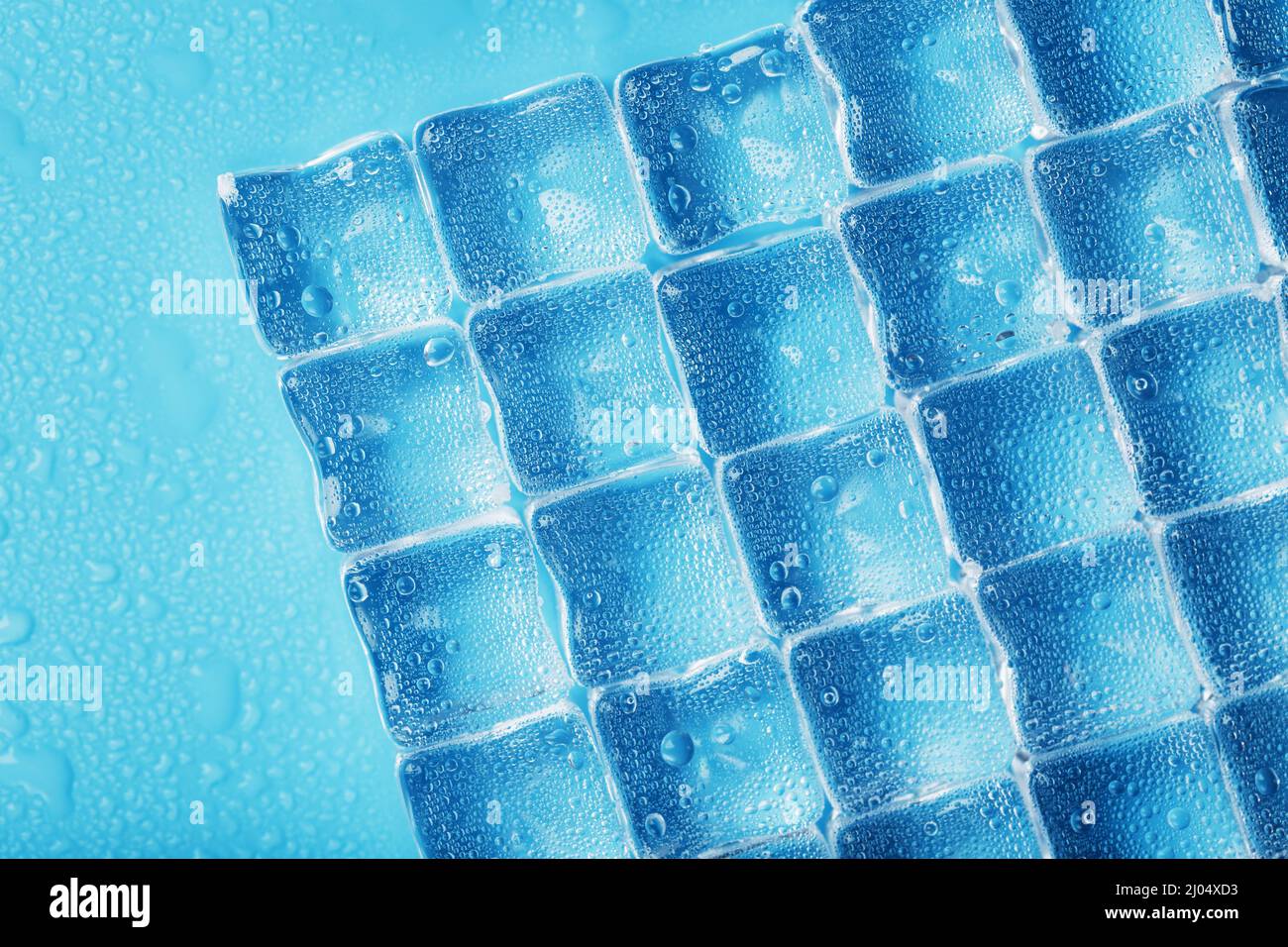Ice cubes with water drops scattered on a blue background, top view ...