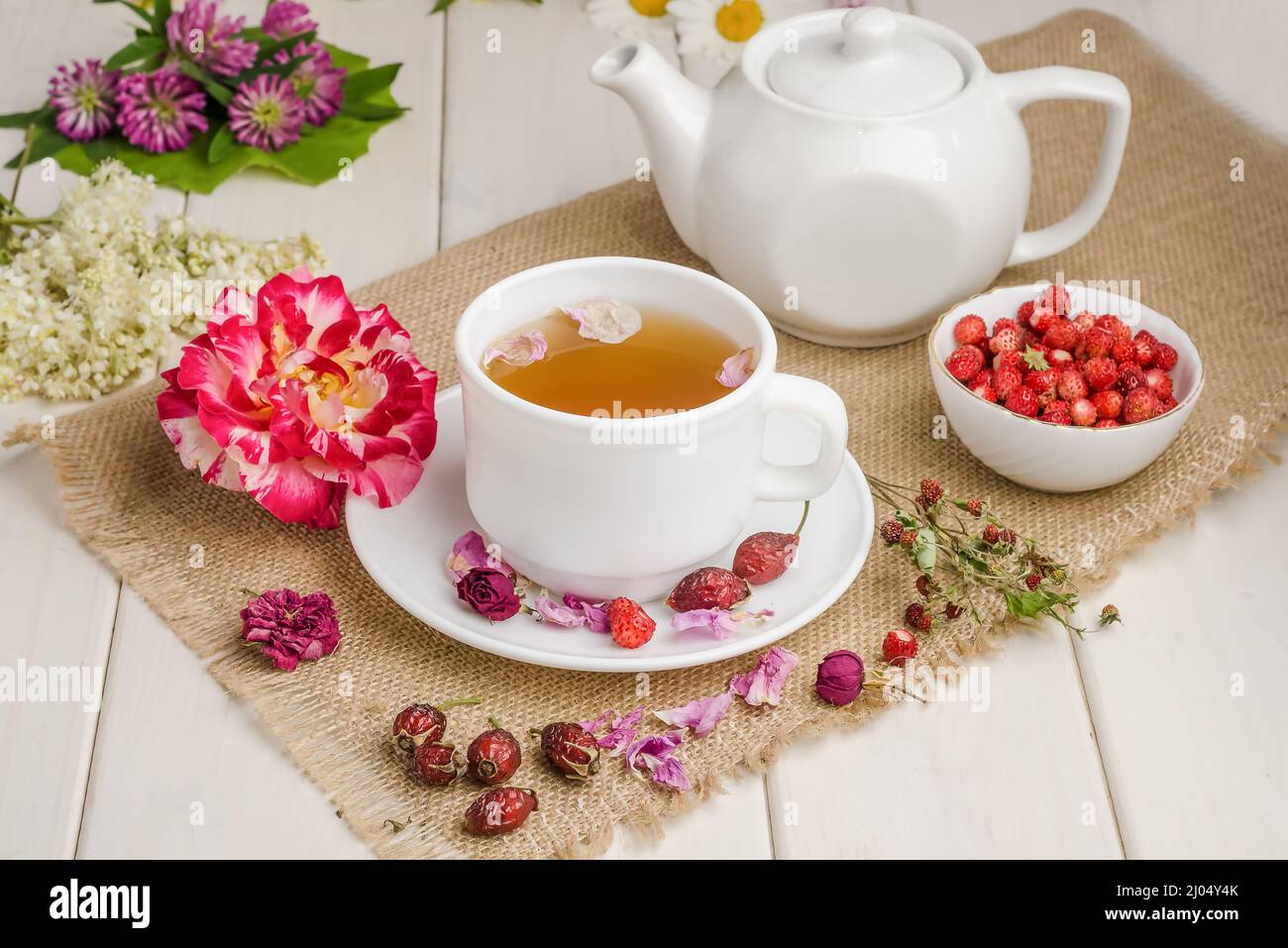 Herbal tea with rosehip, chamomile and meadowsweet in a white cup on a white wooden table with flowers. Stock Photo