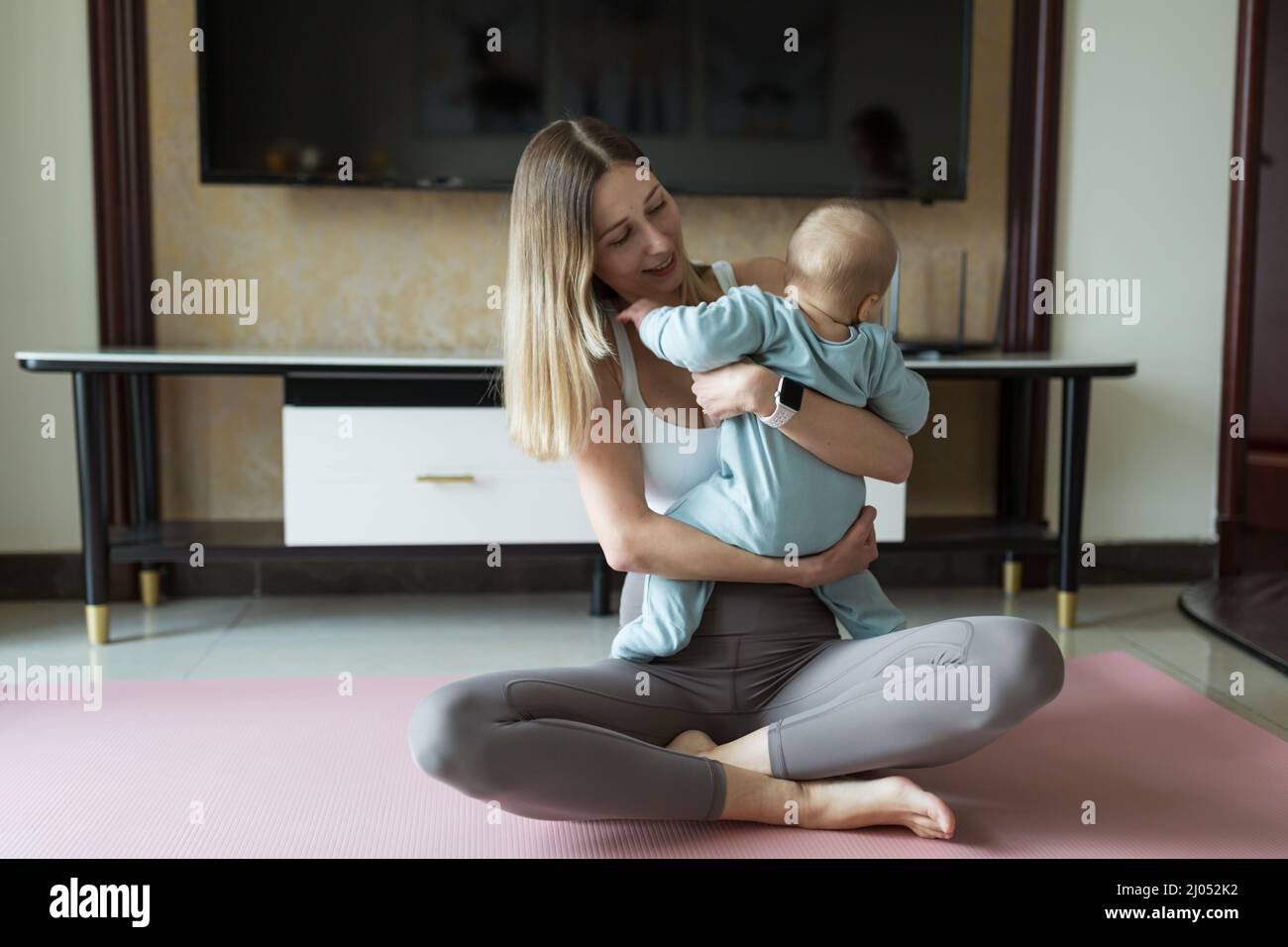 Young mother in sport clothing exercising at home with baby. Online