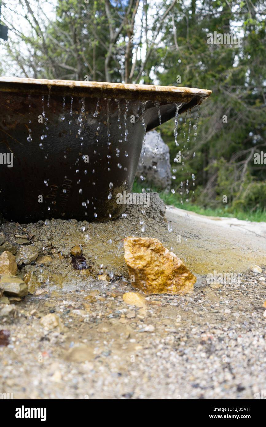 Water drops falling on sand from an old black metal bathtub with green