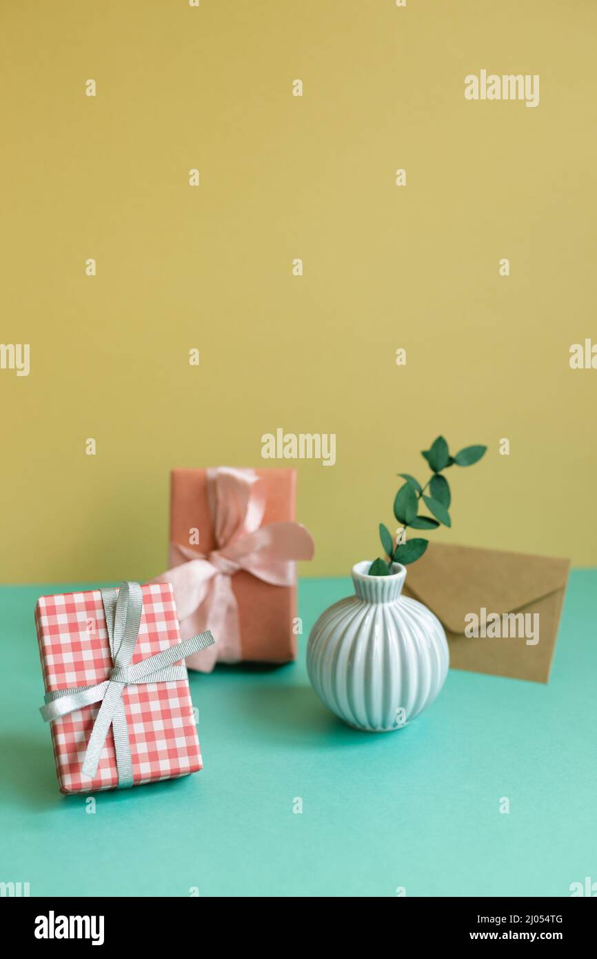 Gift box, plant, envelope on green table. yellow wall background Stock Photo