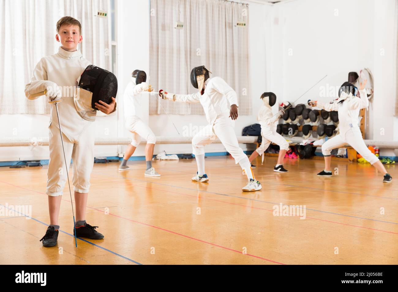 Portrait of teen fencer posing with rapier during fencing class in