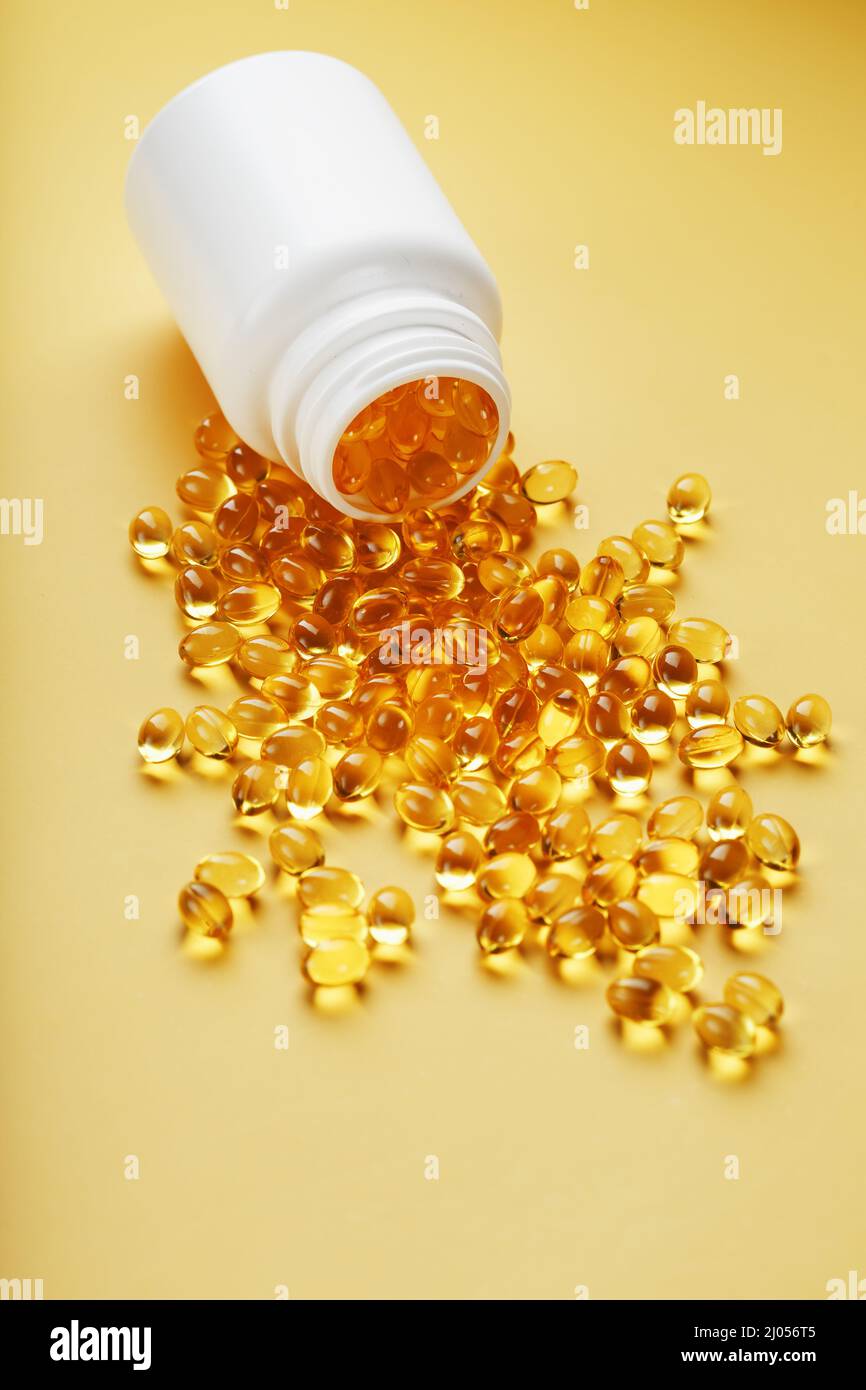 Gold Vitamin D3 capsules poured out of a jar on a yellow background