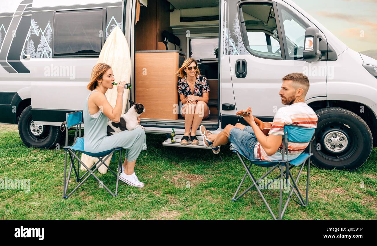 Friends with their dog drinking beer in front of their camper van Stock