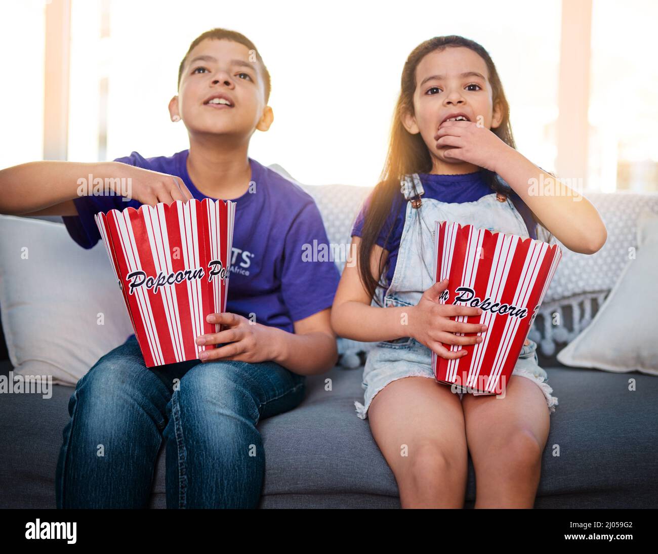 Movie days are always the best. Shot of two young children sitting on a sofa and eating popcorn while watching movies at home. Stock Photo