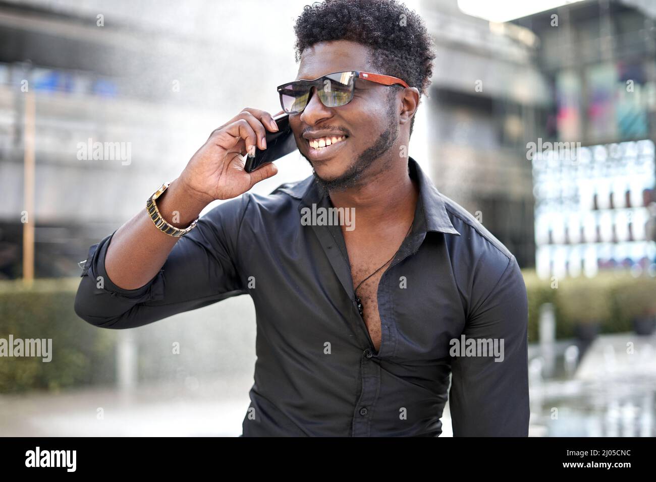 African stylish man talking to the mobile while smiling outdoors Stock Photo