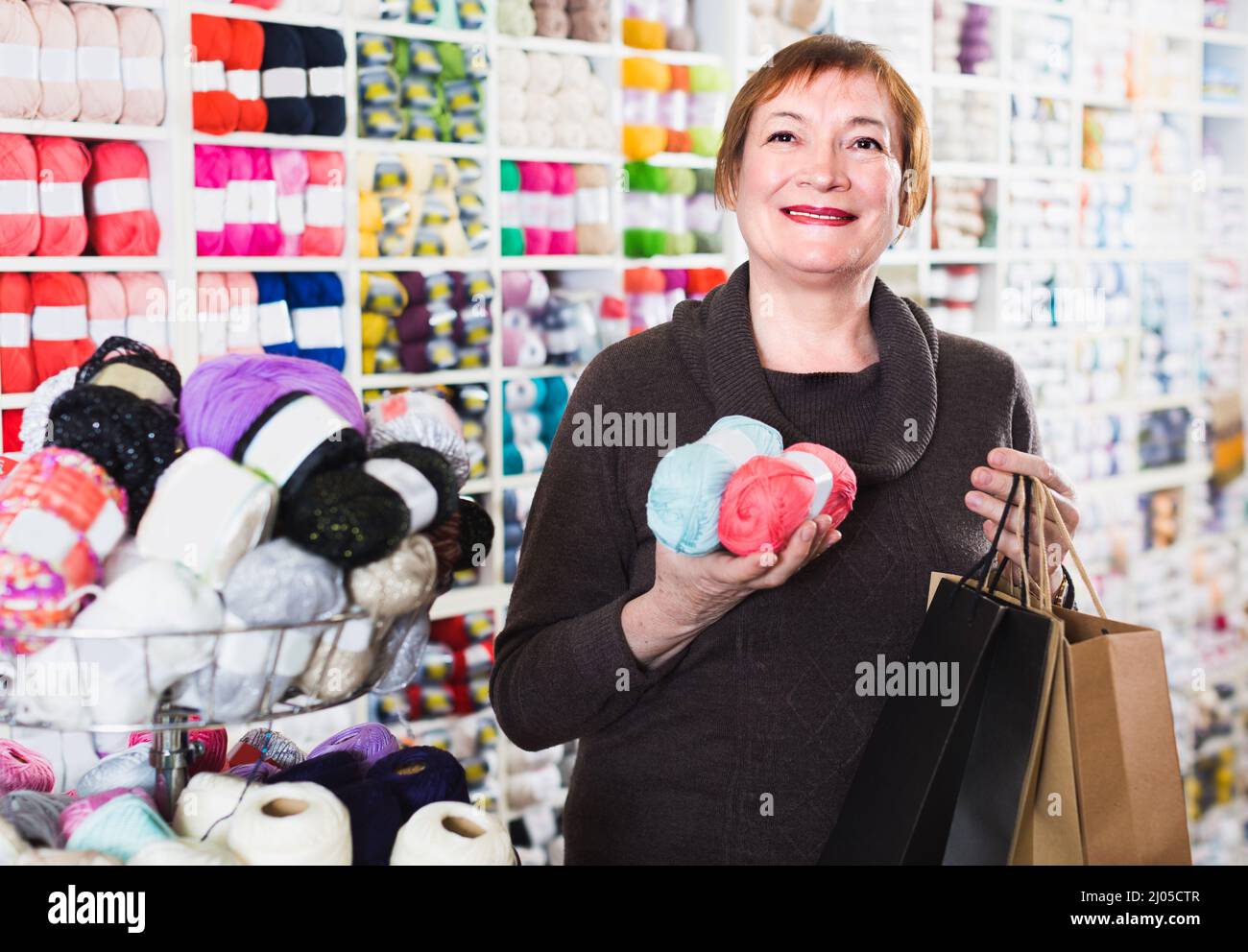 Mature woman is standing in needlework store with shopping bags Stock