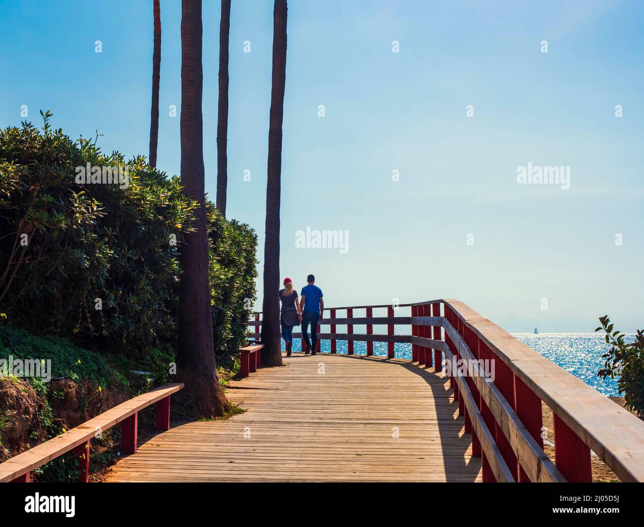 Couple walking in front of the sea along the wooden path of the coastal path of Mijas on a sunny winter day. Stock Photo