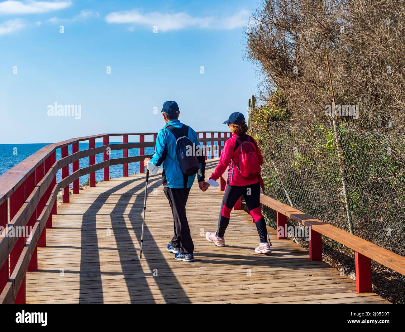 Couple walking in front of the sea along the wooden path of the coastal path of Mijas on a sunny winter day. Stock Photo