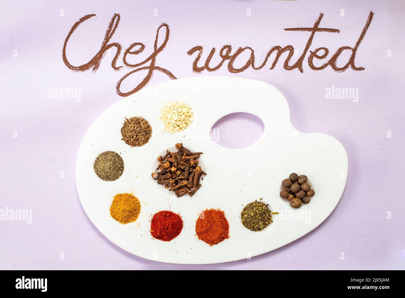 Chef wanted handwritten on purple paper with brown chalk, next to a painter's palette with condiments as painting colors (paprika, curcuma, all spice, Stock Photo