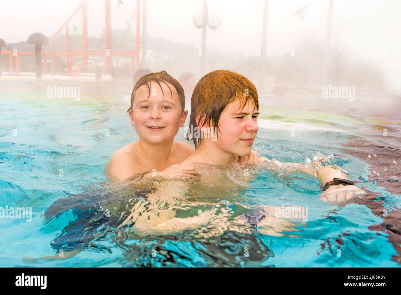 brothers are swimming in the outside area of a thermic pool in Wintertime in warm water, it is foggy Stock Photo