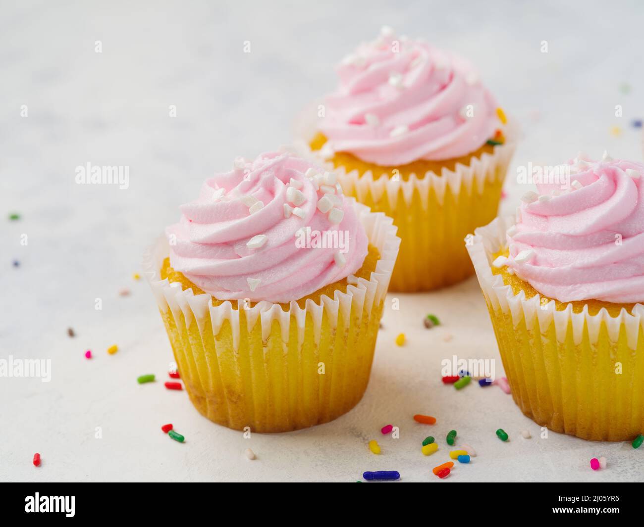 Multi-colored confetti are scattered on a white background. Cupcakes with cream. Sweet food, holiday. Restaurant, hotel, cafe, culinary blog, pastry s Stock Photo