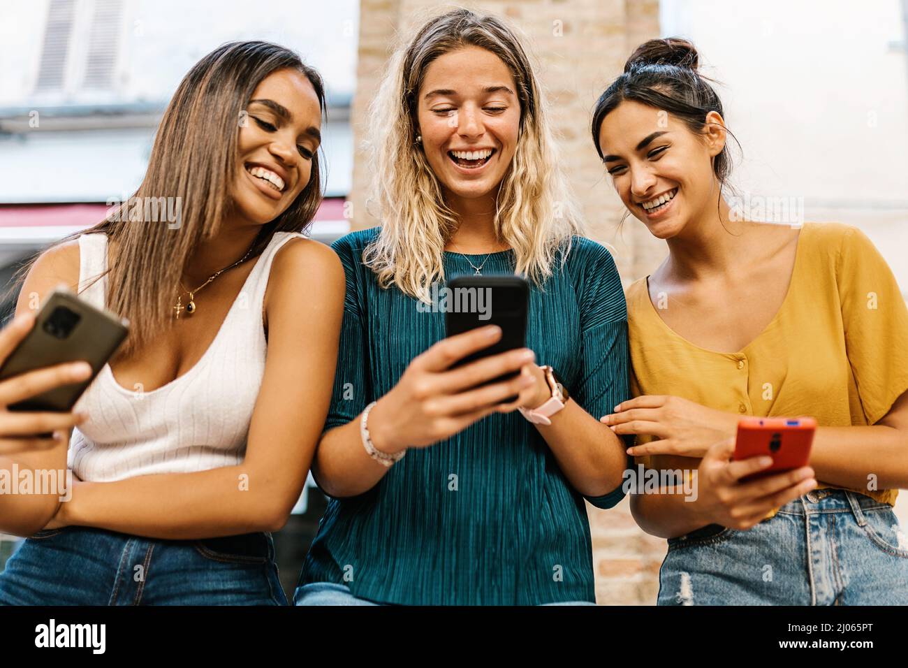 Smiling multiethnic female friends having fun together using mobile phone Stock Photo