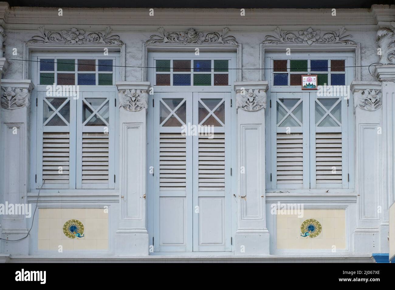 Light blue Straits Chinese Peranakan shophouse with wooden louver shutters, rococo floral designs, peacock mosaic tiles & feng shui mirror with Bagua Stock Photo