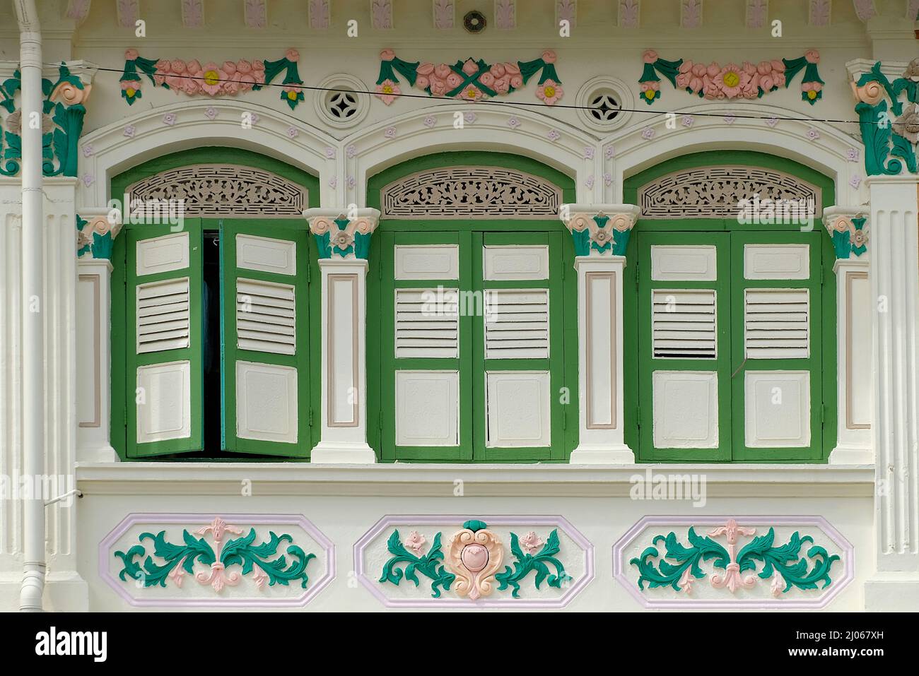 Beige Straits Chinese Peranakan shophouse with olive green wooden louvered shutters, rococo floral designs & Bagua feng shui mirror above frame Stock Photo