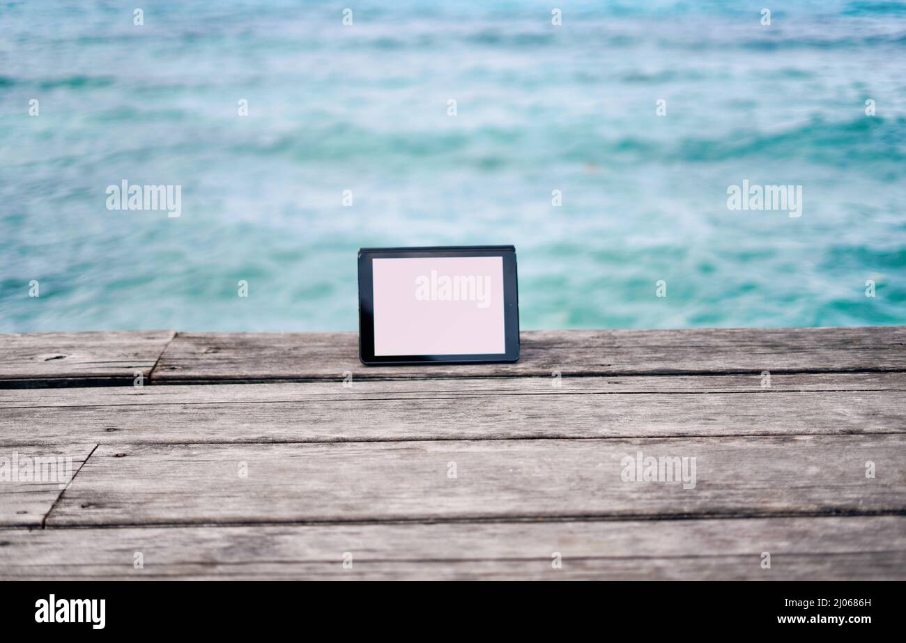 Stay in the loop wherever you travel in life. Still life shot of a digital tablet placed on a boardwalk overlooking the ocean in Raja Ampat, Indonesia Stock Photo