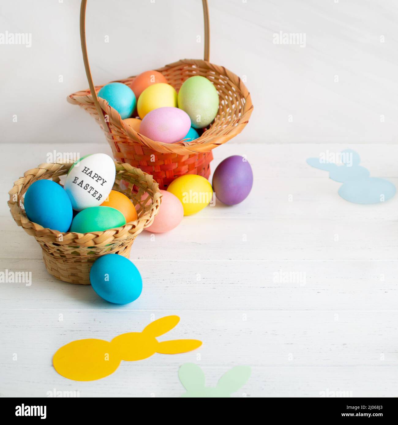 Many colorful Easter eggs in wicker basket with paper bunnies garland