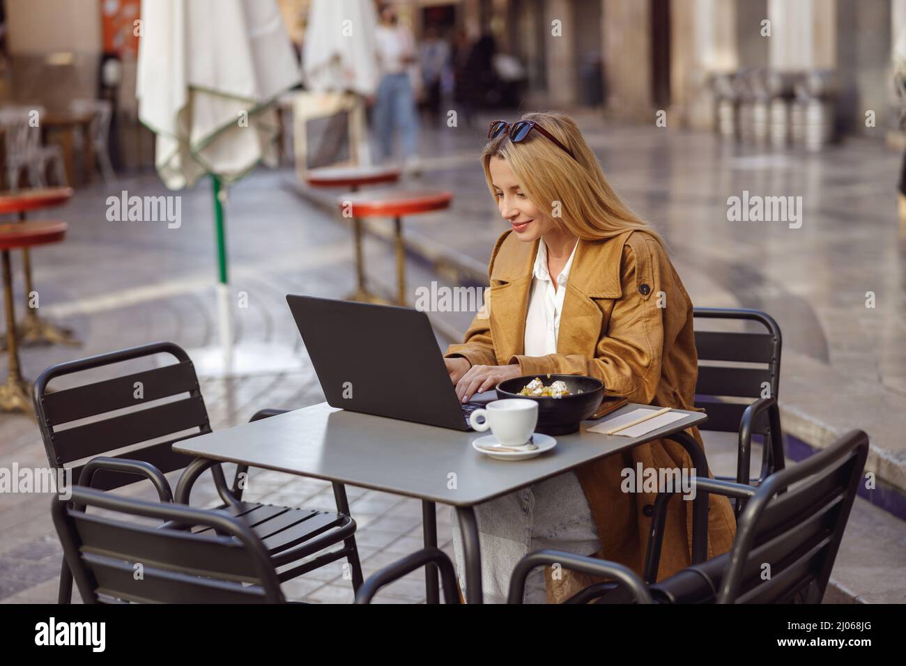 Focused woman sitting at table in street cafe, working on laptop Stock Photo