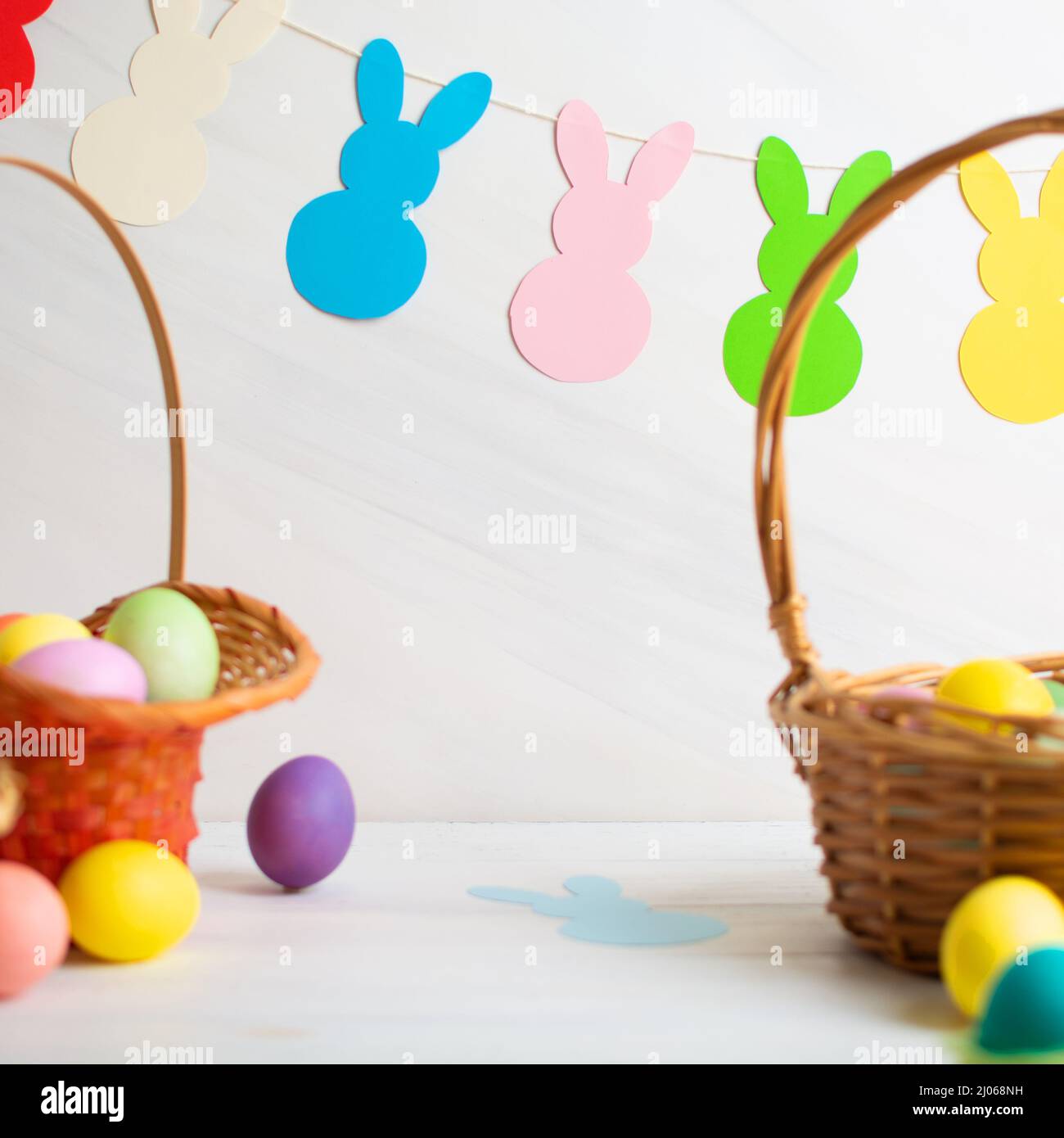 Many colorful Easter eggs in wicker basket with paper bunnies garland Stock Photo