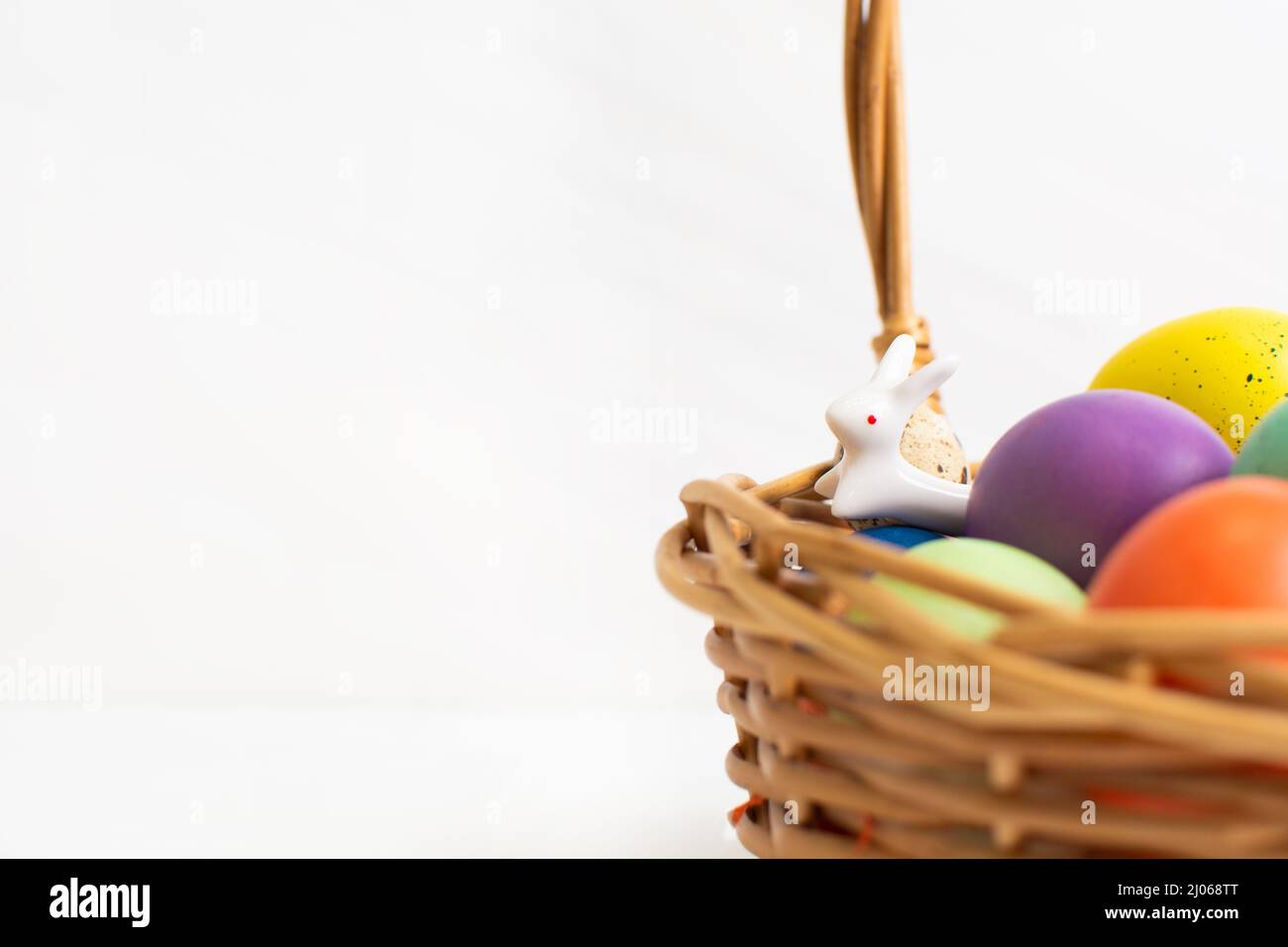 Colorful Easter eggs in wicker basket with ceramic bunny. Happy Easter ...