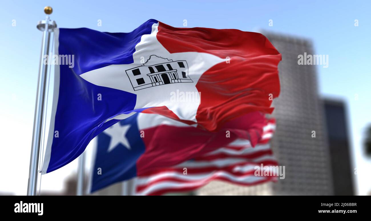 San Antonio city flag waving in the wind with Texas state and United States national flags blurred in background. Black-outlined Alamo in the middle o Stock Photo