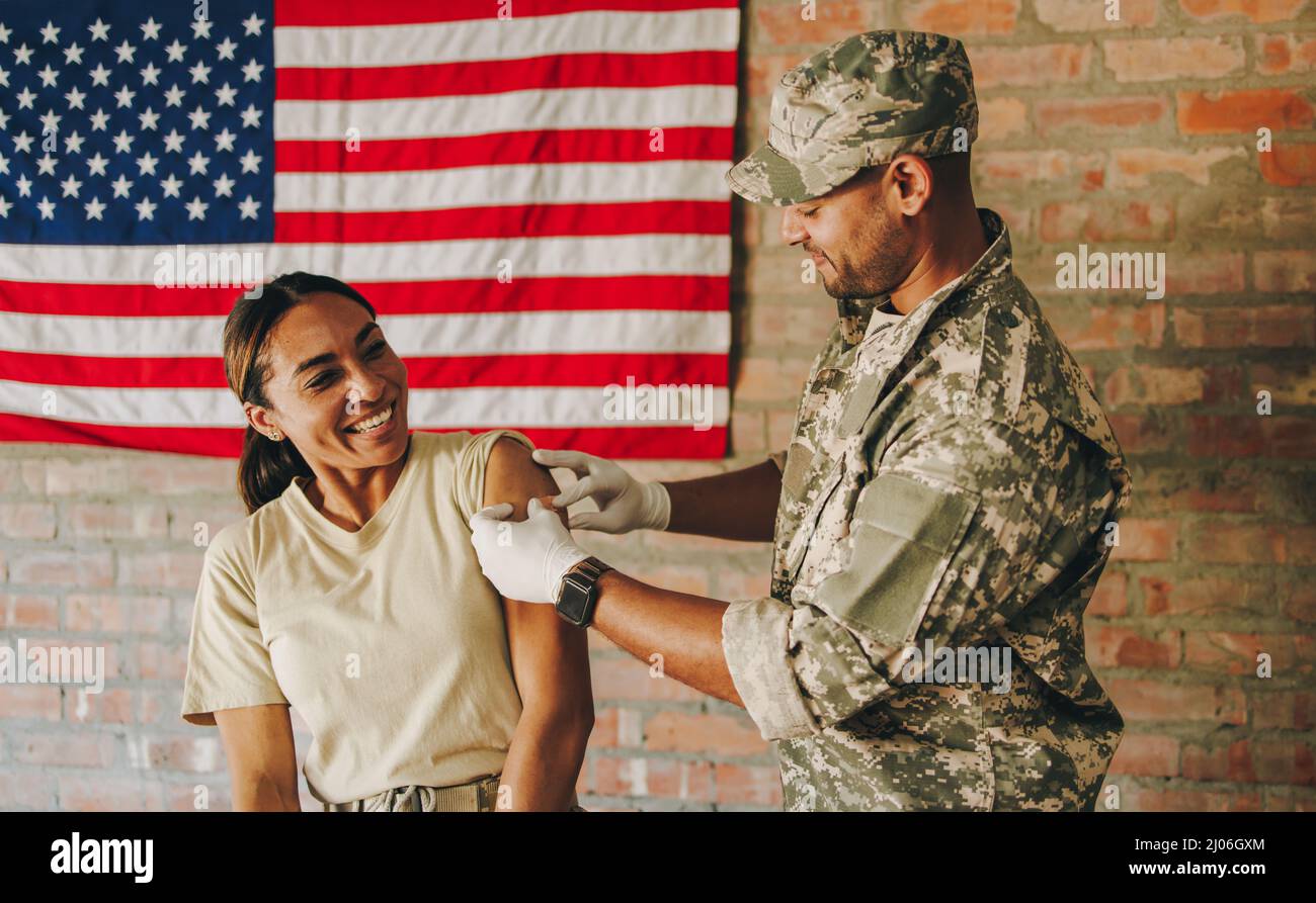 Young medic placing a band aid on a soldier's arm in the military hospital. American military physician applying a medical adhesive after administerin Stock Photo