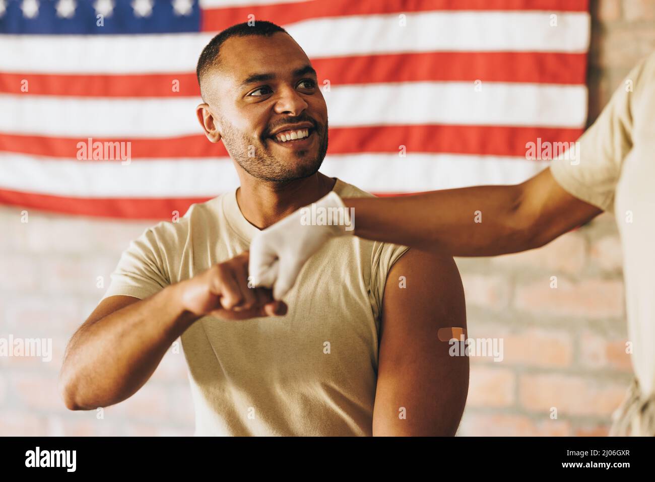 Cheerful young soldier fist bumping a medic after getting vaccinated in the military clinic. American serviceman being congratulated by a nurse after Stock Photo