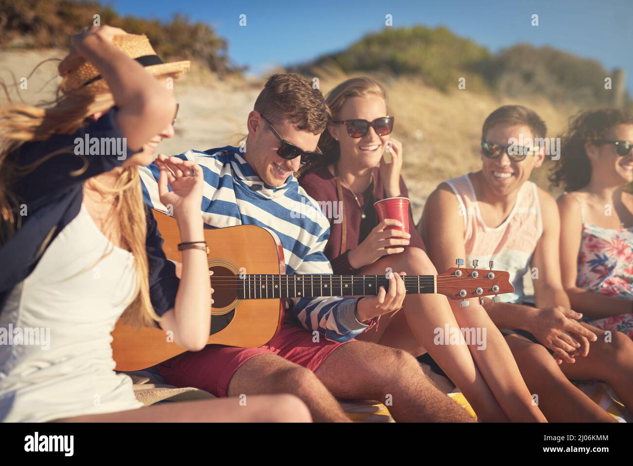 His music brings them happiness. Cropped shot of a handsome young man playing a guitar for his friends on a summers day at the beach. Stock Photo