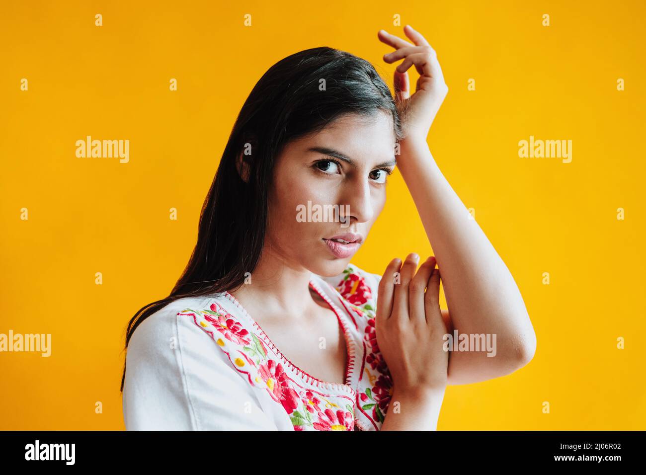 portrait of young hispanic woman with mexican traditional dress and copy space on yellow background in Mexico Latin America Stock Photo
