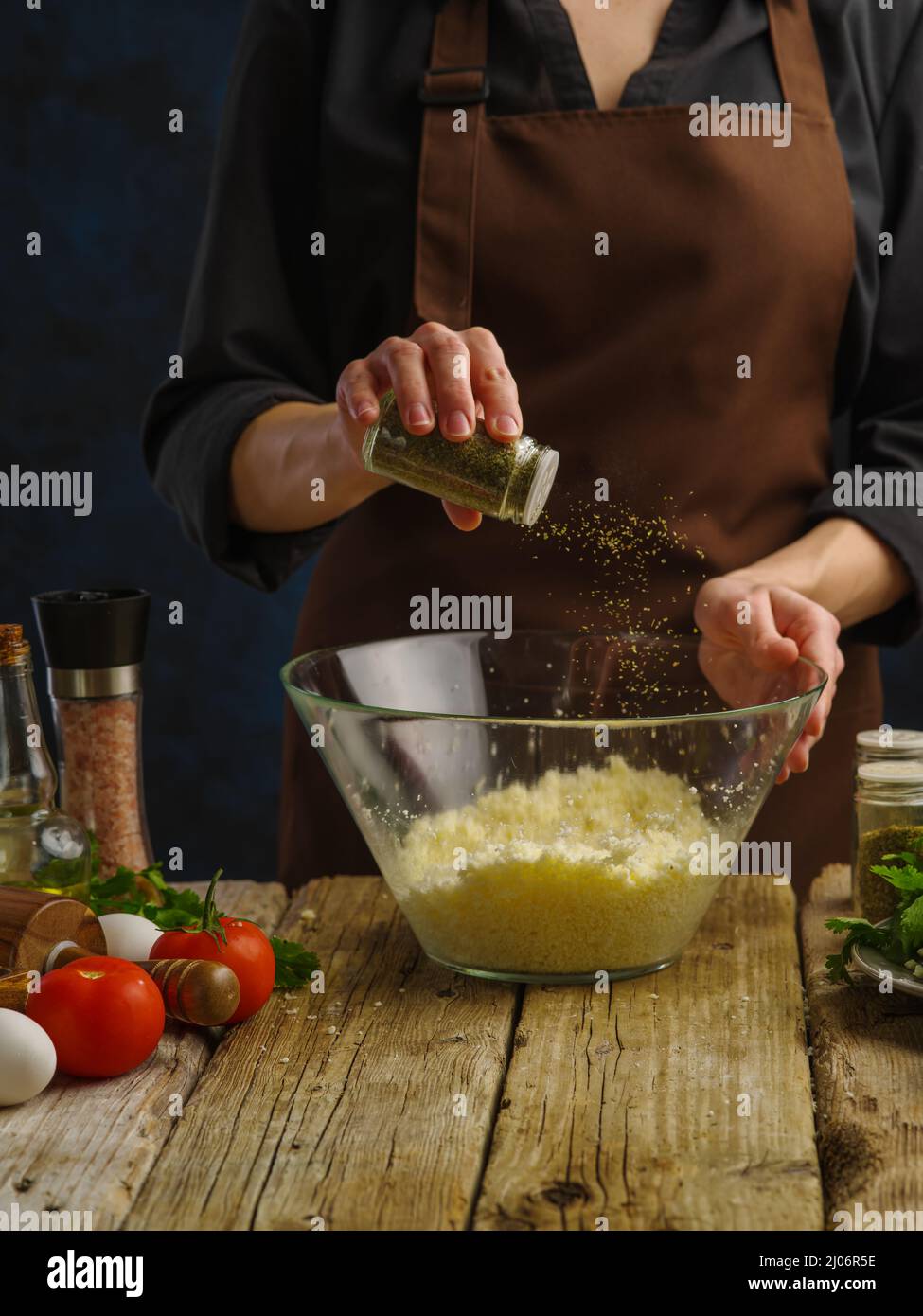 The chef adds spices to the grated cheese. Vegetables, herbs, spices on a wooden table. Cooking dishes with cheese - pizza, spaghetti, sauce, pasta, s Stock Photo