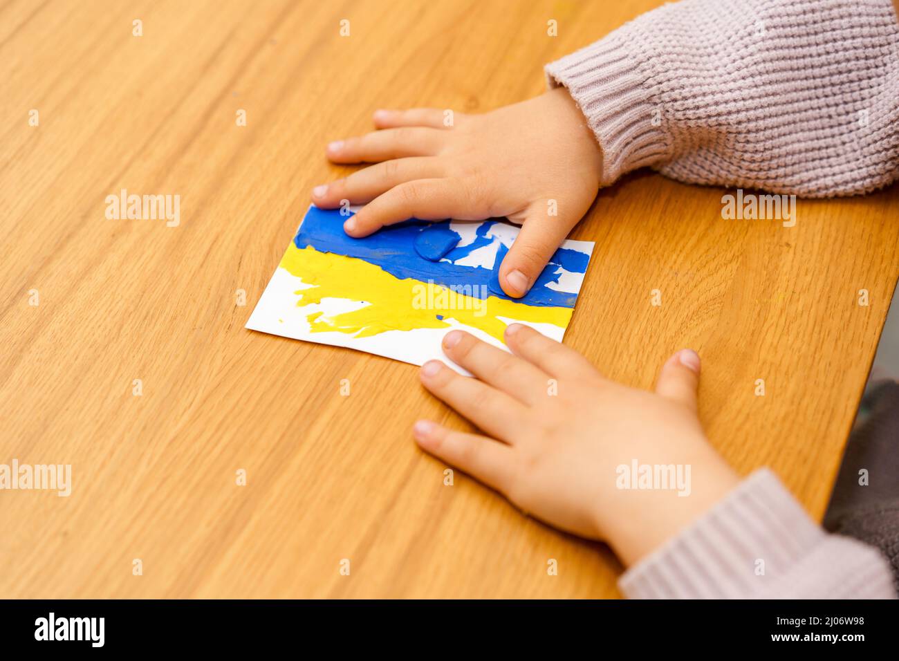 Support for Ukraine. Close up little child hands modeling Ukraine flag from blue and yellow color plasticine. Concept of patriotism, respect, charity, help, solidarity with the citizens of Ukraine. Stock Photo