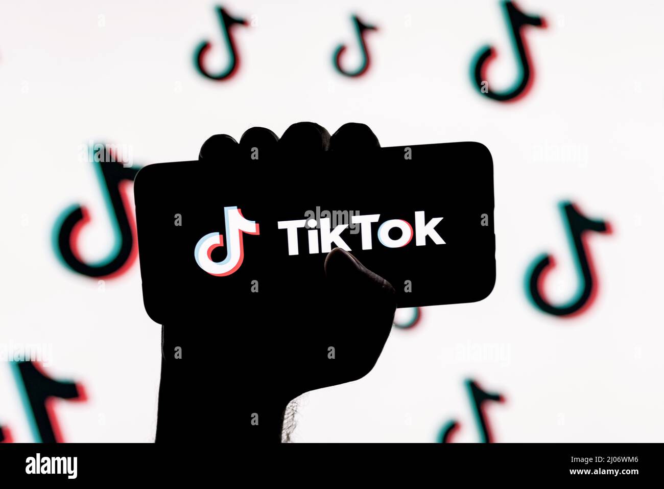 Smartphone with the TikTok social network logo on the screen in a clenched hand on the background of TikTok logos Stock Photo