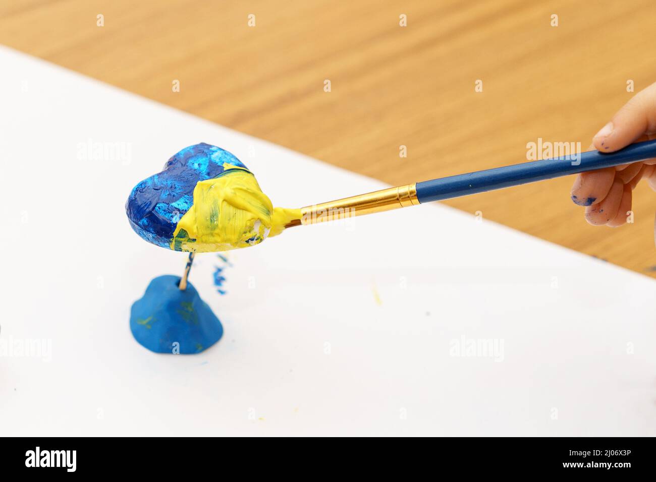 The child draw national flag of Ukraine painted yellow and blue on heart shape. The concept of patriotism, respect, support, help and solidarity with the citizens of Ukraine. Stock Photo