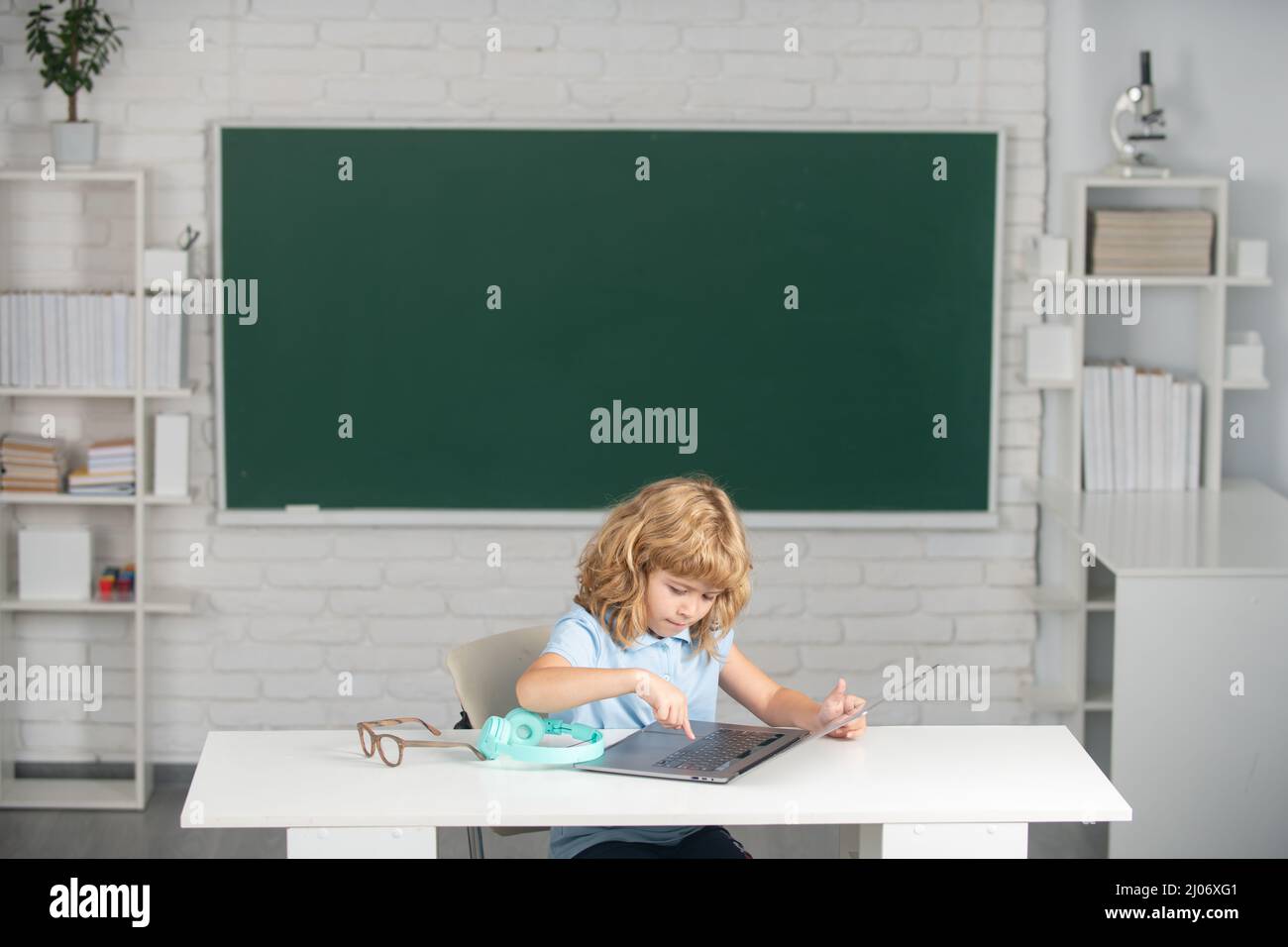 School child using digital pc laptop in class. Portrait of funny pupil of primary school study programming. Stock Photo