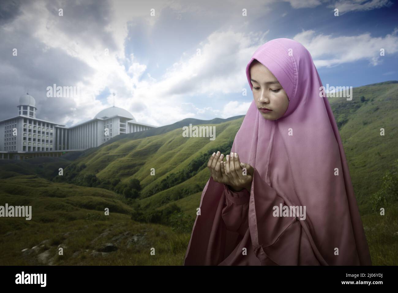 Asian Muslim woman in a veil standing while raised hands and praying ...