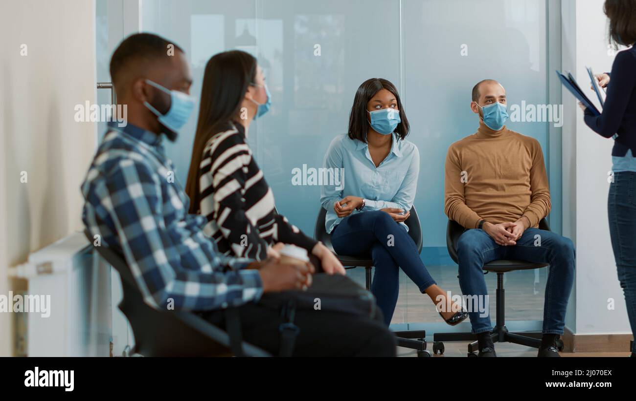 HR employee giving resume files - Hr Employee Giving Resume Files To Diverse Group Of Candidates Waiting In Queue To Attend Job Interview Meeting Applicants With Cv Papers Sitting In Lobby During Covid 19 Pandemic 2J070EX 