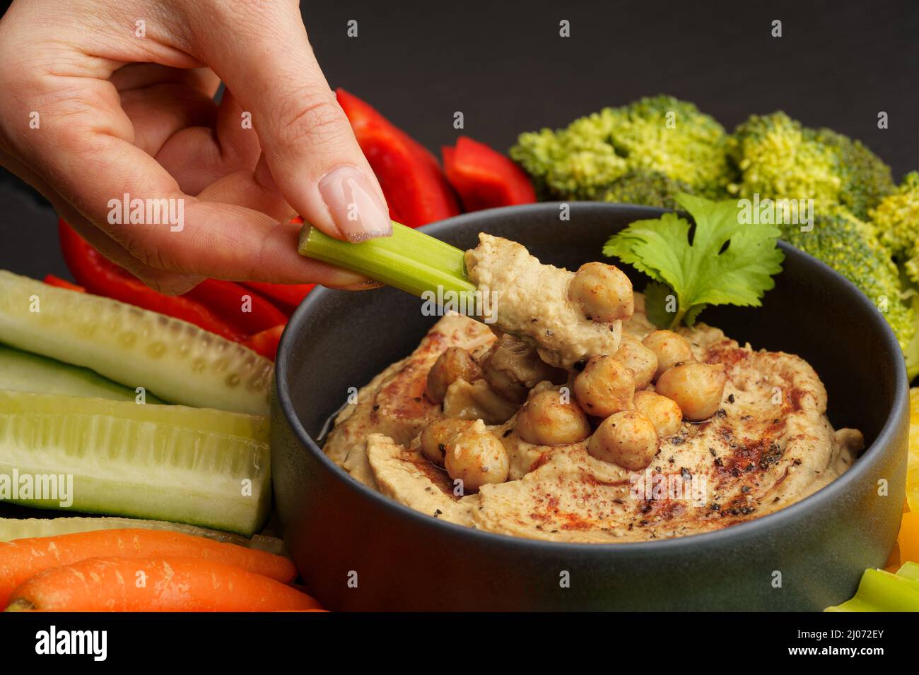 Woman hand taking chickpeas hummus with celery stick. Tasty hummus with fresh vegetables Stock Photo